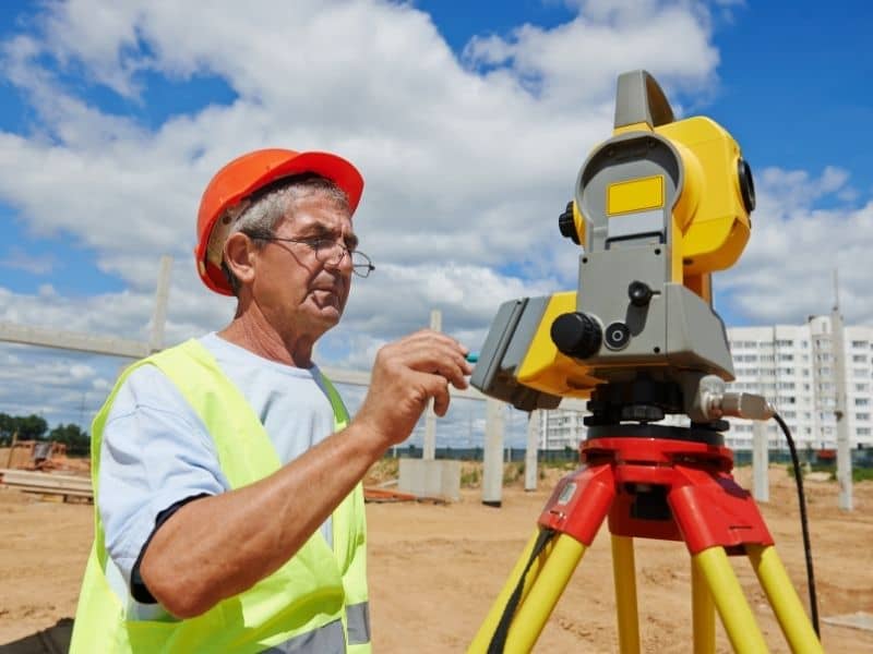 Licensed land surveyor using a total station to collect precise property measurements during an ALTA Survey before a commercial real estate transaction.