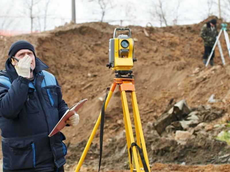 Surveyor measuring hillside slope conditions to guide building placement, driveway access, and grading plans